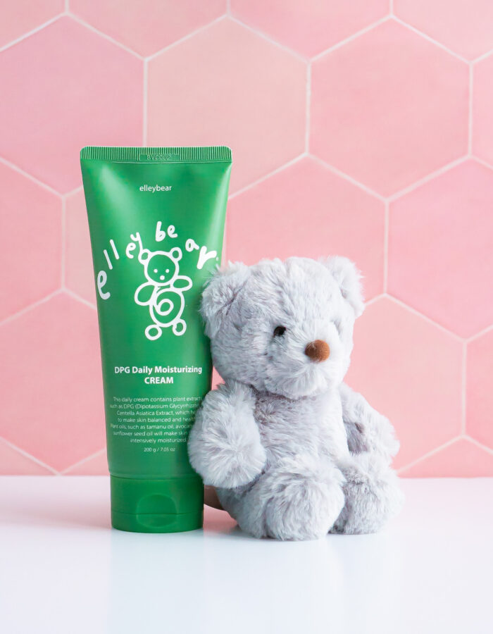 DPG Daily Moisturizing Cream - 200g Green tube ona pink tile background with a grey teddy bear