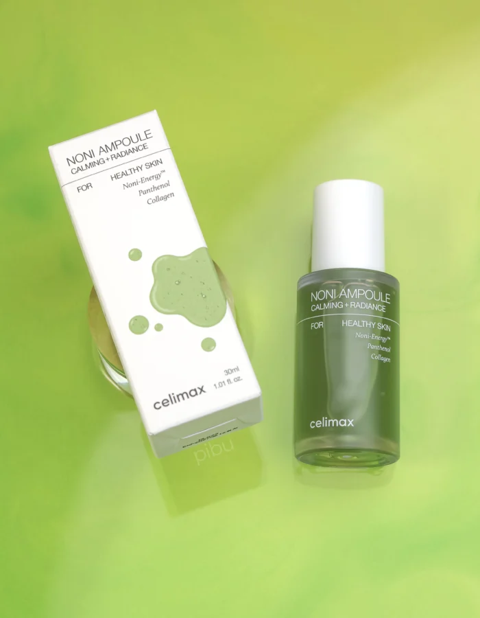 A green serum bottle and box labeled Celimax The Real Noni Energy Ampoule Calming + Radiance on a vibrant green background.