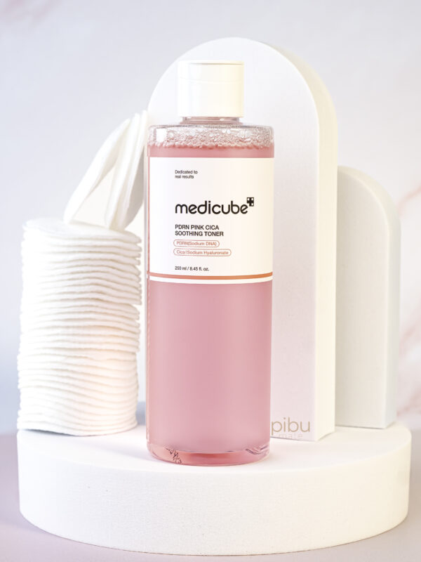 Medicube pdrn pink cica soothing toner Standing on white round platform with cotton round pads on the side
