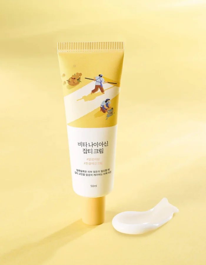 A tube of cream with a yellow design and illustrations, placed on a yellow background, next to a small dollop of cream.