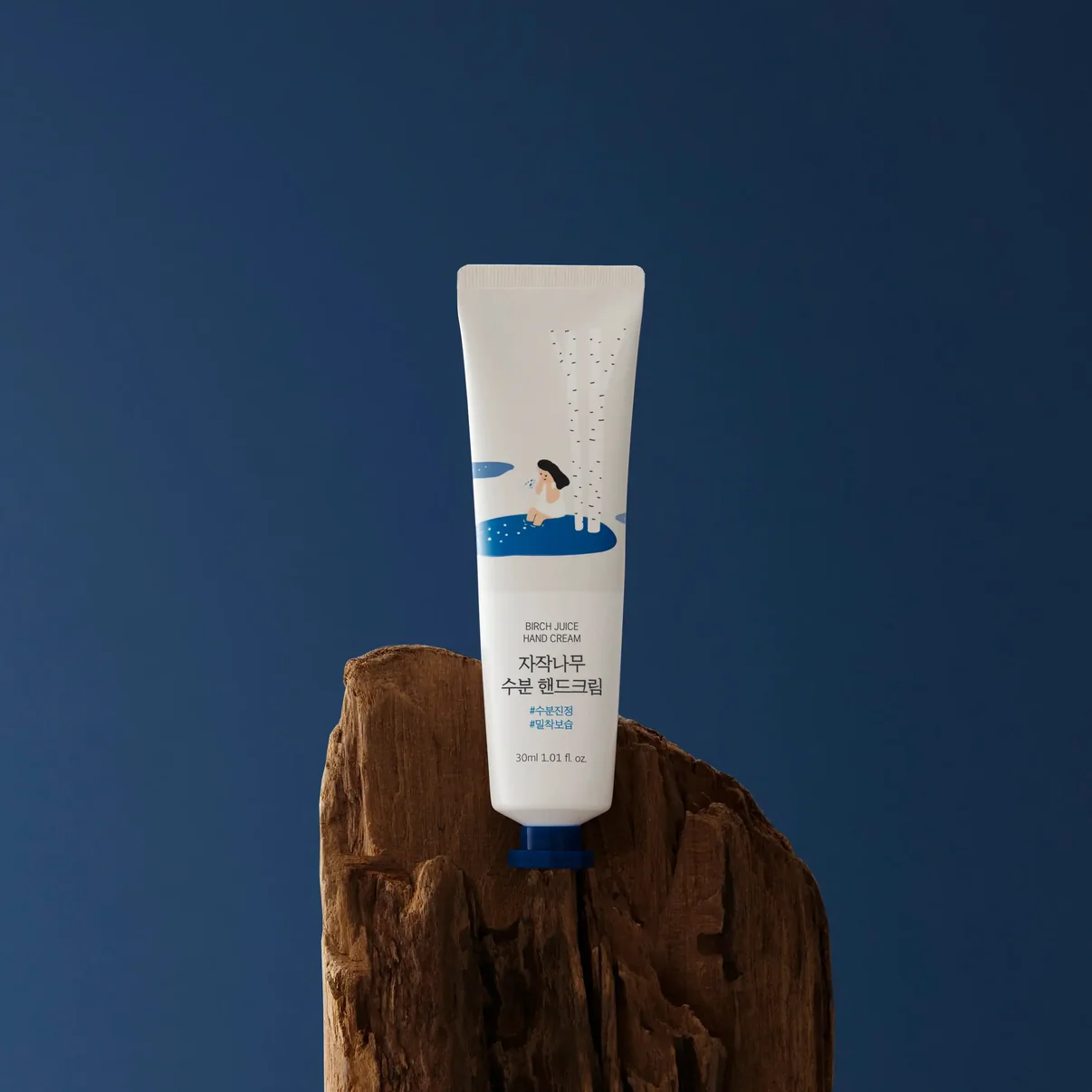 A tube of birch juice hand cream resting on a wooden surface against a dark blue background.