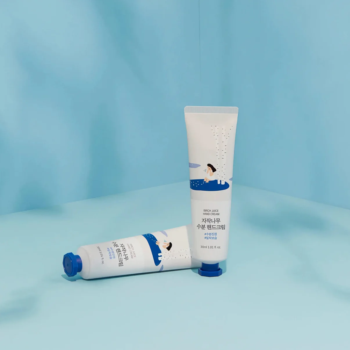 Two tubes of birch hand cream on a light blue background, featuring playful illustrations and product details.