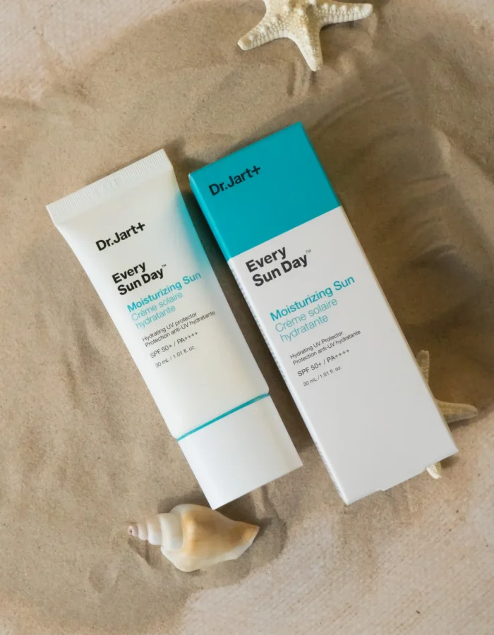 Two tubes of Dr. Jart Every Sun Day moisturizing sunscreen on sandy surface with seashell and starfish.
