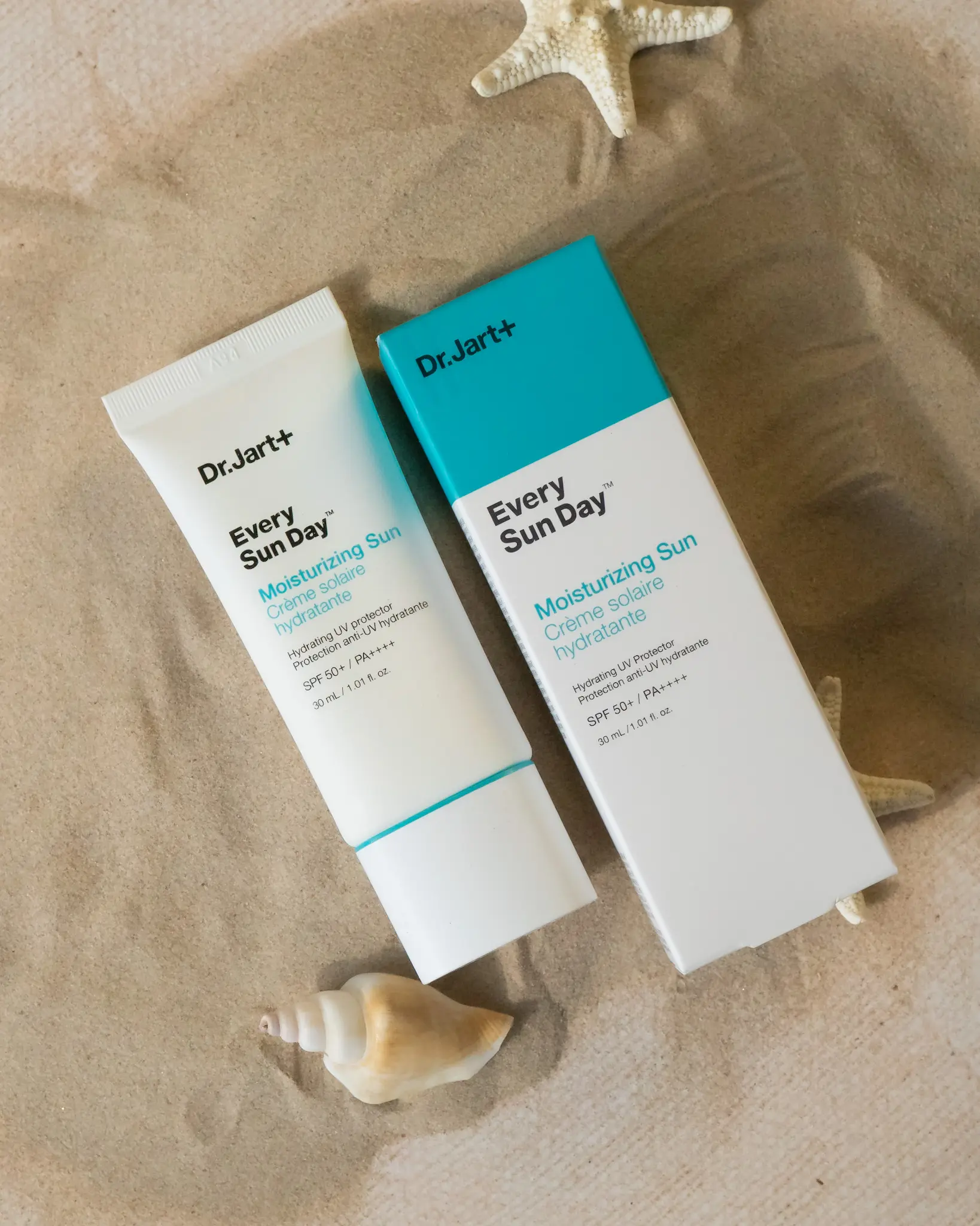 Two tubes of Dr. Jart Every Sun Day moisturizing sunscreen on sandy surface with seashell and starfish.
