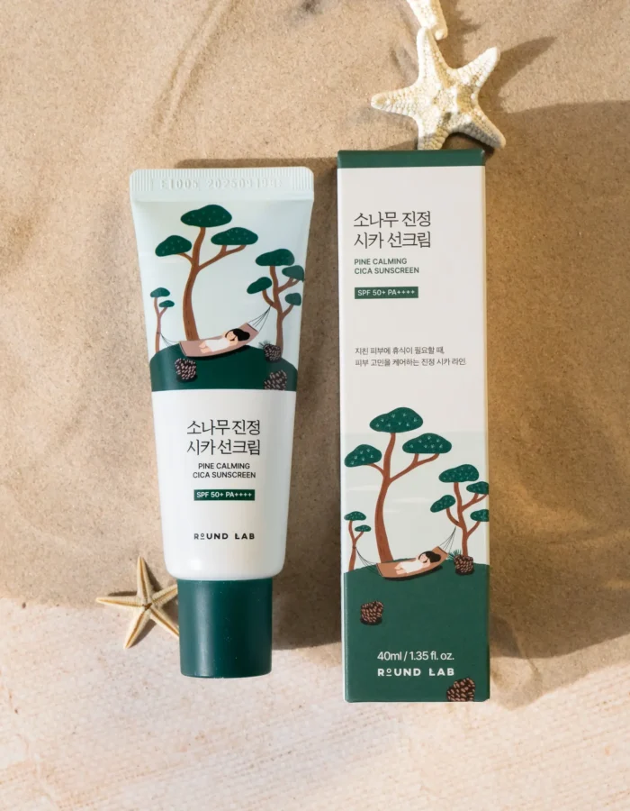 Round Lab Pine Calming Cica sunscreen tube and box on sandy surface, featuring illustrations of trees and a hammock.