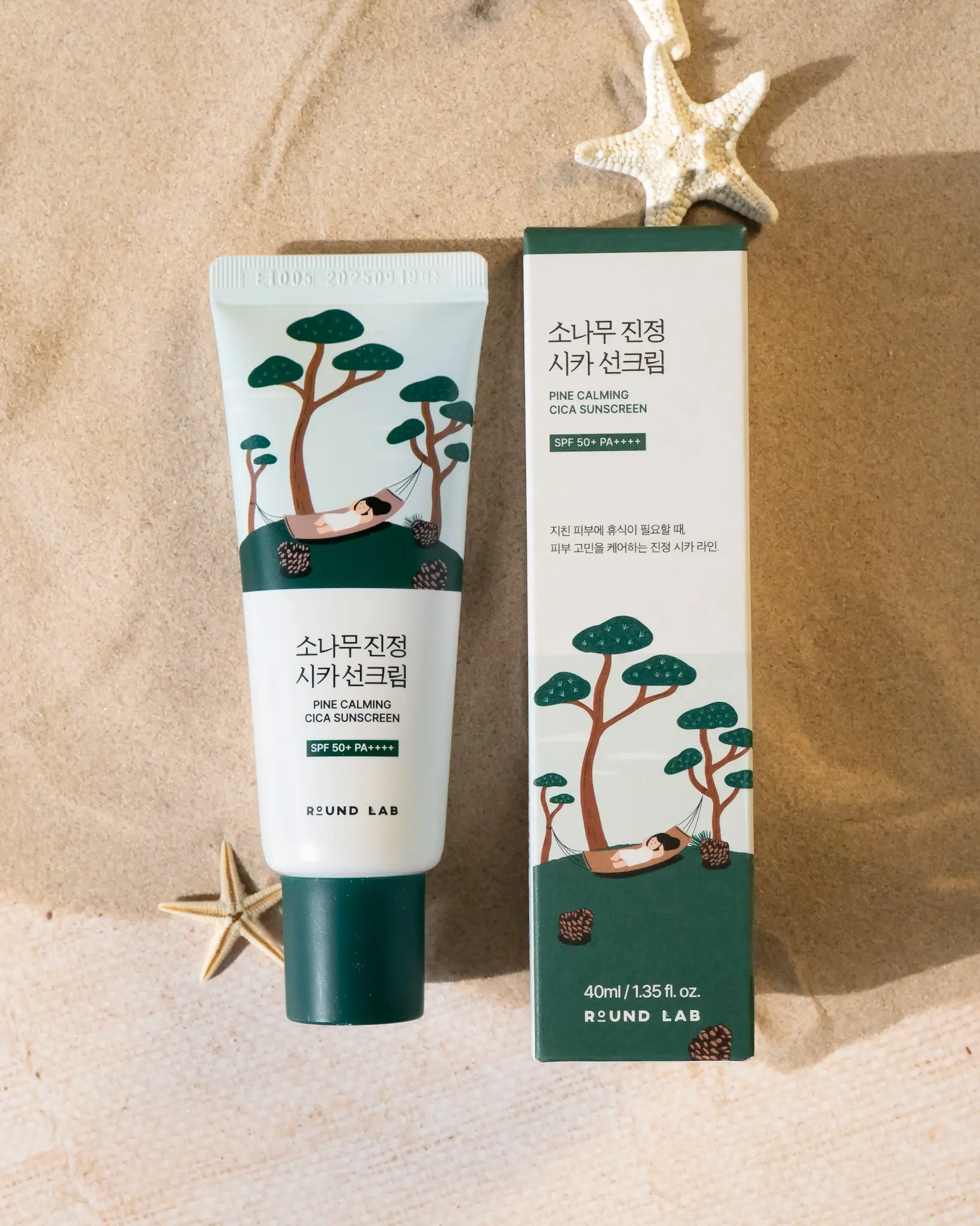 Round Lab Pine Calming Cica sunscreen tube and box on sandy surface, featuring illustrations of trees and a hammock.
