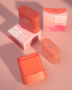 Two Kaja Dewy Bar Cheek Lip Multi Balms and their packaging on a soft pink background.