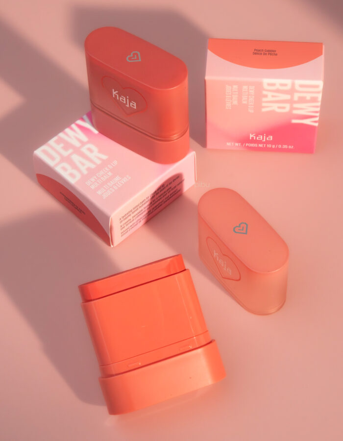 Two Kaja Dewy Bar Cheek Lip Multi Balms and their packaging on a soft pink background.
