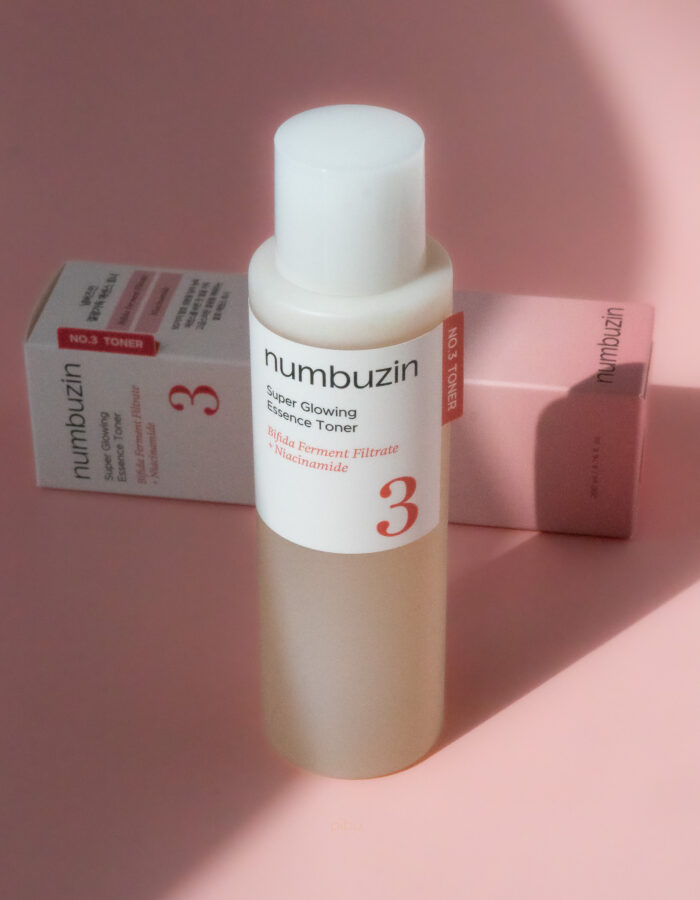 Bottle of Numbuzin No. 3 Super Glowing Essence Toner with packaging, set against a soft pink background.