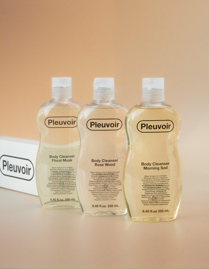 Three Pleuvoir body cleanser bottles labeled Floral Musk, Rose Wood, and Morning Soil on a soft gradient background.