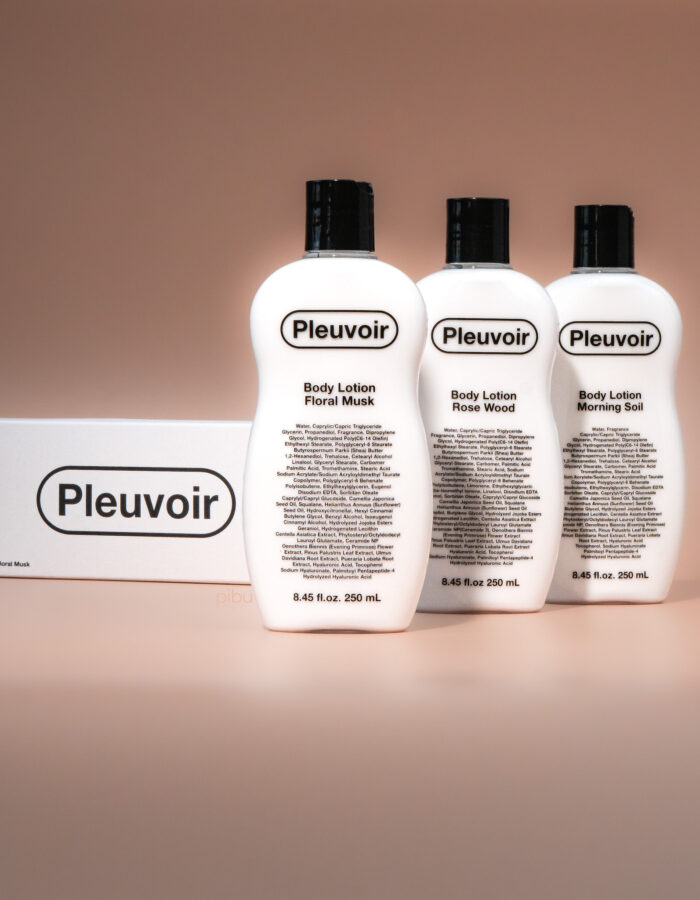 Three Pleuvoir body lotion bottles labeled Floral Musk, Rose Wood, and Morning Soil, displayed with a box on a soft backgroun
