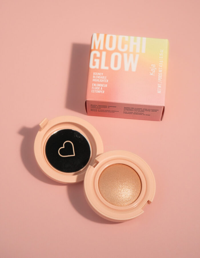 Open compact of Kaja Mochi Glow highlighter in Luna, featuring a shimmery gold shade and a pink box in the background.